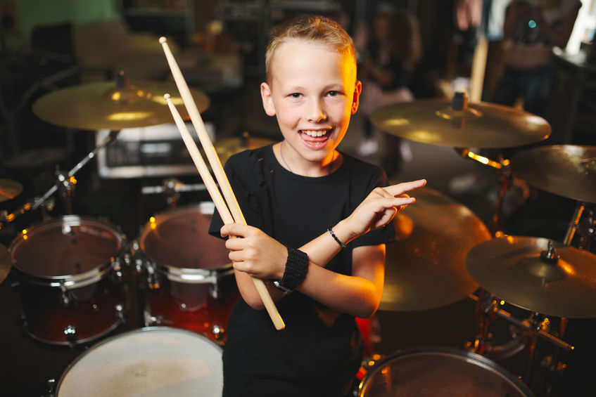 A happy student at a drum kit holding drumsticks